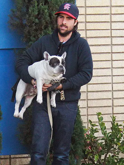 Jason Schwartzman outdoors while carrying a French Bulldog