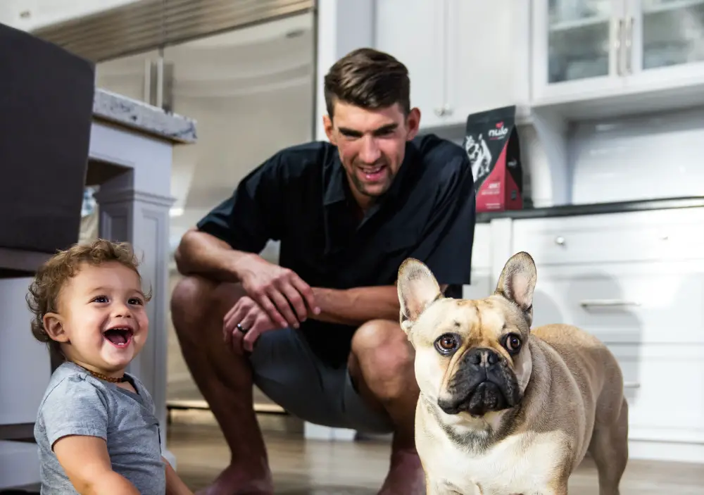 Michael Phelps behind his kid and French Bulldog on the floor