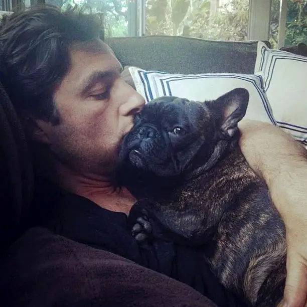 Zach Braff lying on the couch while kissing his French Bulldog lying on top of him