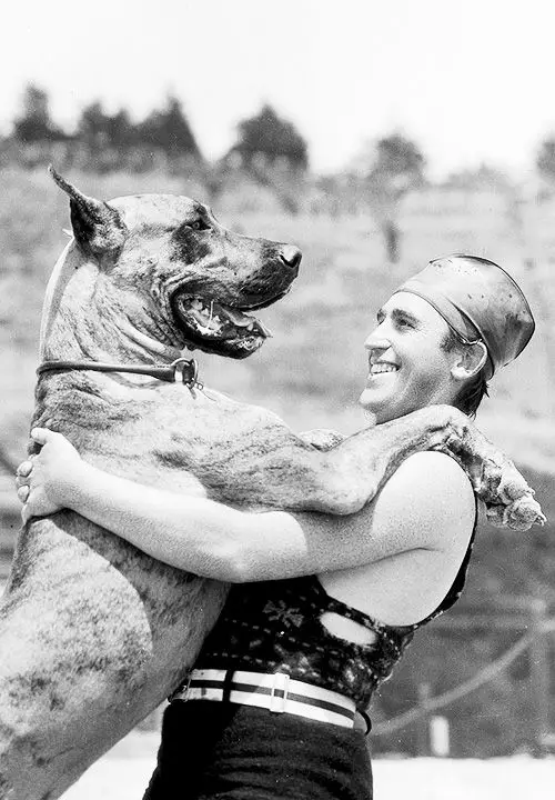 a black and white photo of Harold Lloyd hugging his standing up Great Dane dog