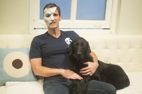 Hugh Panaro wearing a mask and sitting on the couch with his black labradoodle