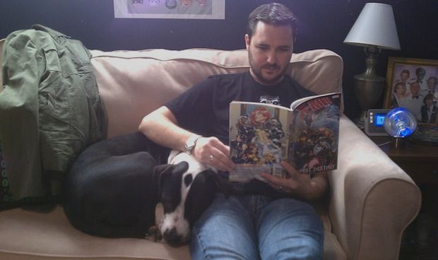 Wil Wheaton on the couch reading a book with its Pit Bull sleeping beside him