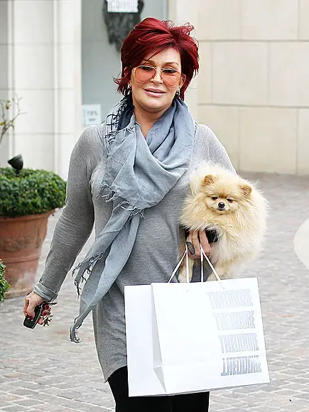 Sharon Osbourne walking in the street with a paper bag in her hand while carrying her Pomeranian