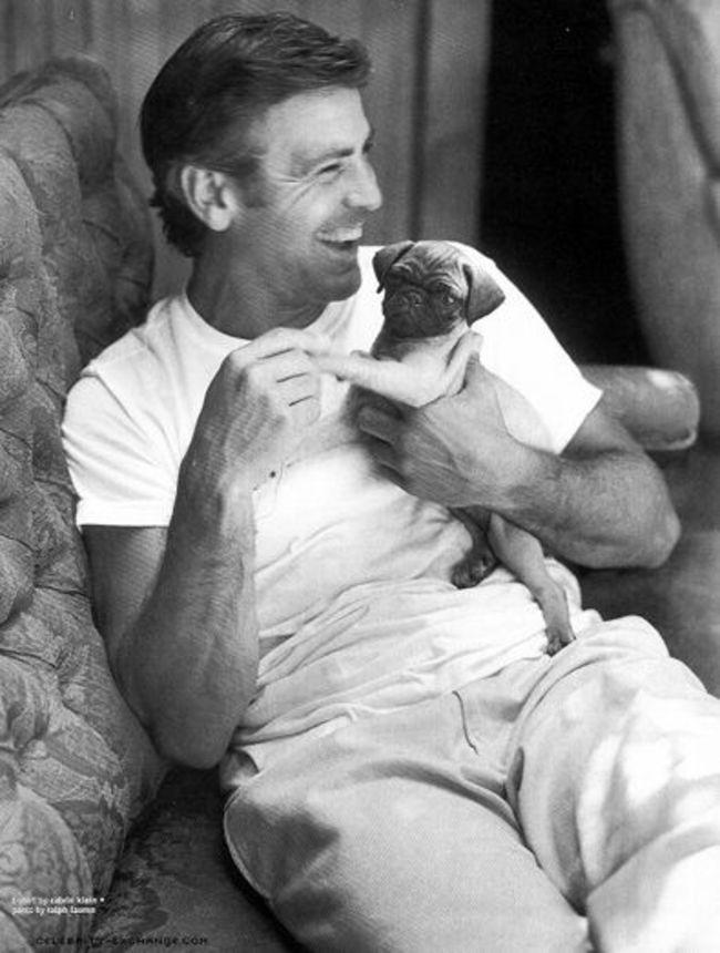 George Clooney sitting on the couch while holding his Pug puppy