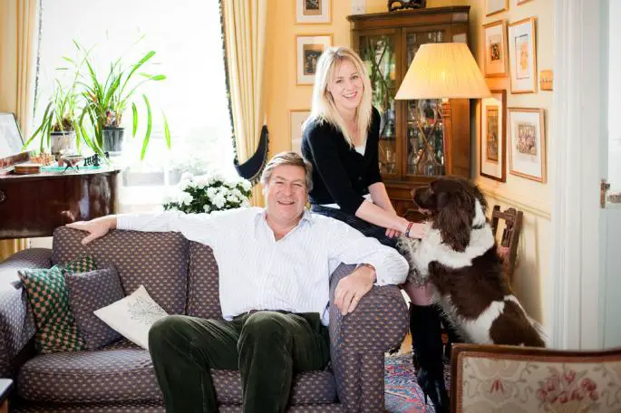 Ed Stourton sitting on the couch while his Springer Spaniel is standing up leaning on a lady beside him