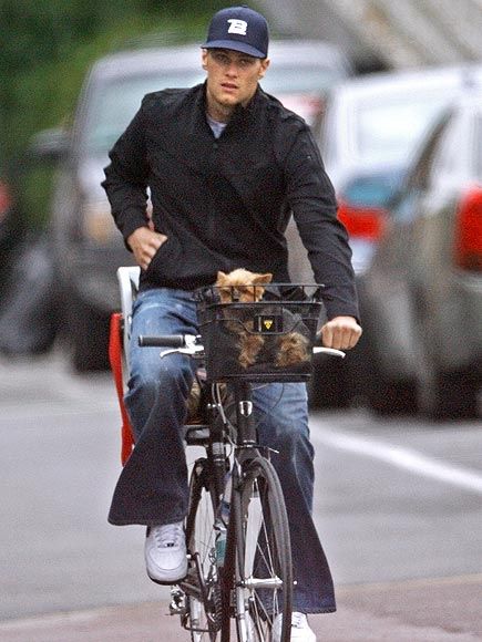 Tom Brady biking in the street with a Yorkie in the basket