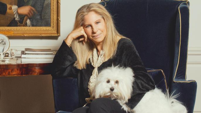 Barbara Striesand sitting on the chair with her Maltese in her lap.