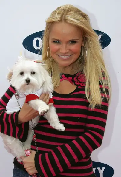 Kristin Chenoweth smiling to the camera while carrying her Maltese named Maddie.