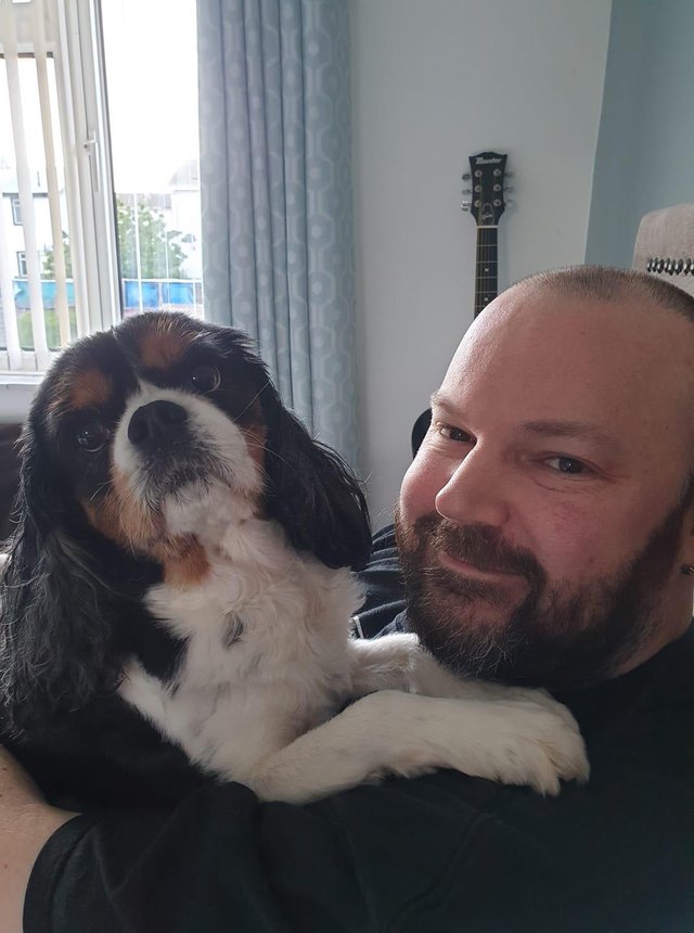 a man hugging a King Charles Spaniel while sitting on the couch