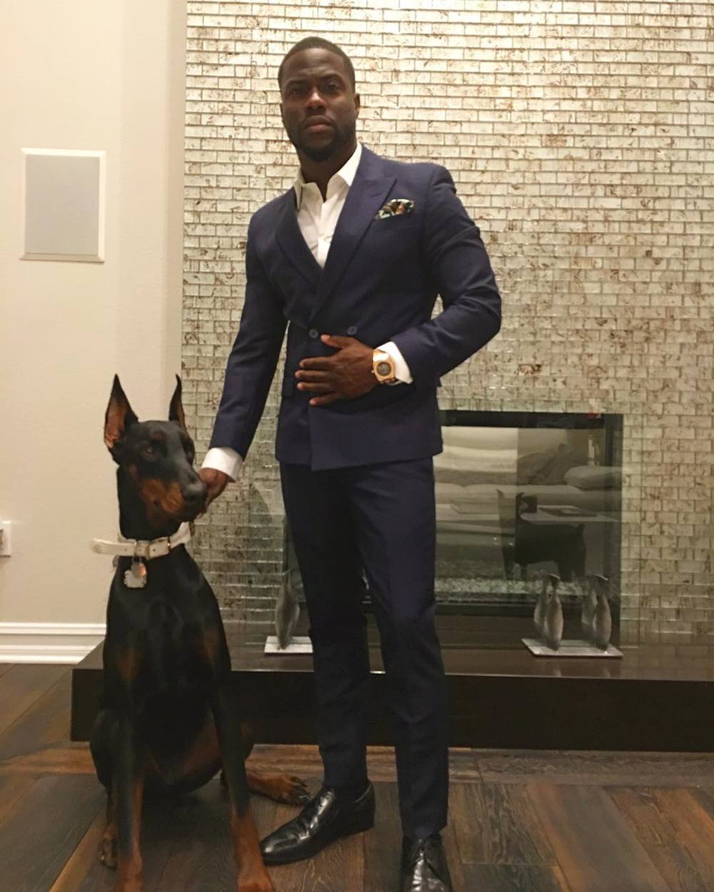 Kevin Hart standing next to his Doberman sitting on the floor