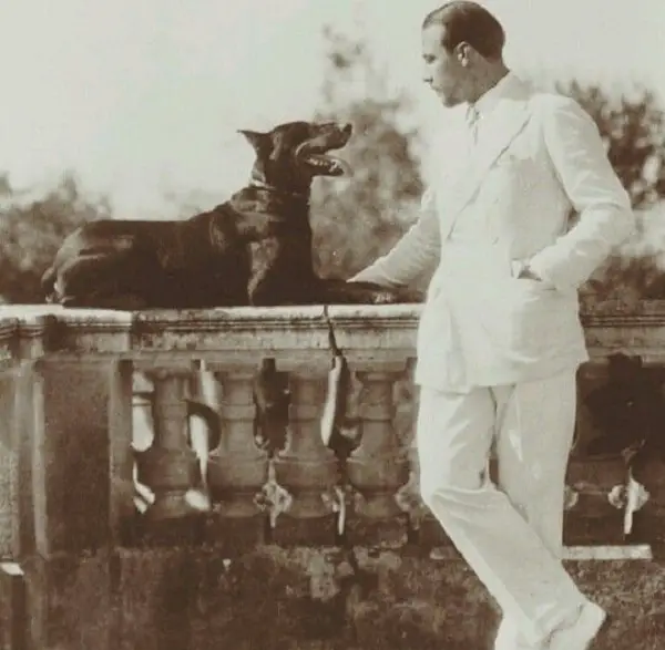 Rudolph Valentino standing in the balcony with his Doberman lying on top of the railings