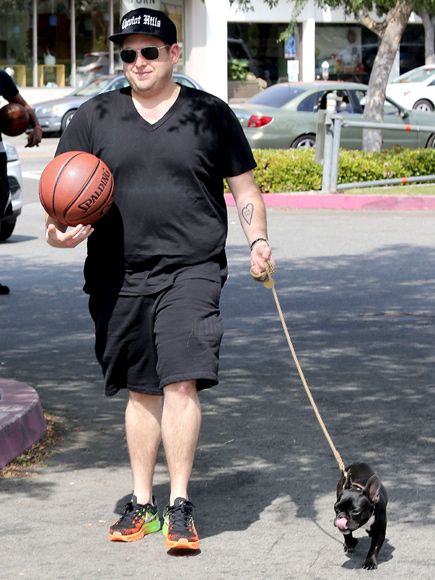 Jonah Hill holding a ball while walking in the street with his French Bulldog on a leash