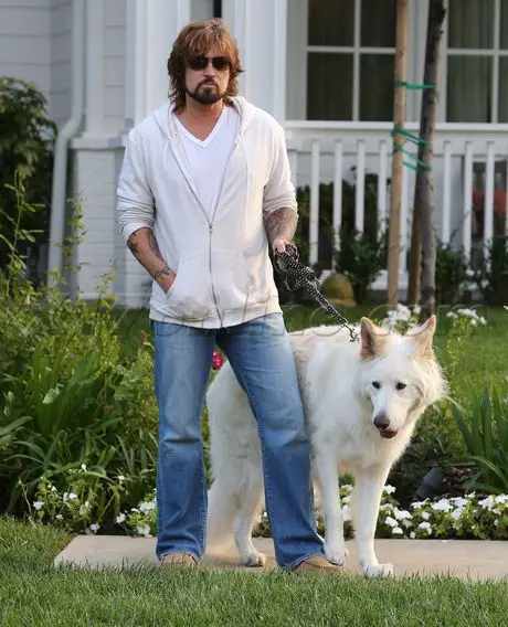 Billy Ray Cyrus standing in the front yard with his German Shepherd next to him