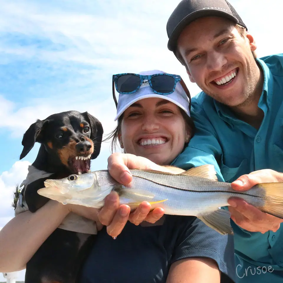 A man and woman showing the fish while their Dachshund is trying to bite it