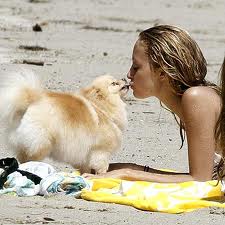 Nickole Richi lying in the sad while kissing her Pomeranian standing across her