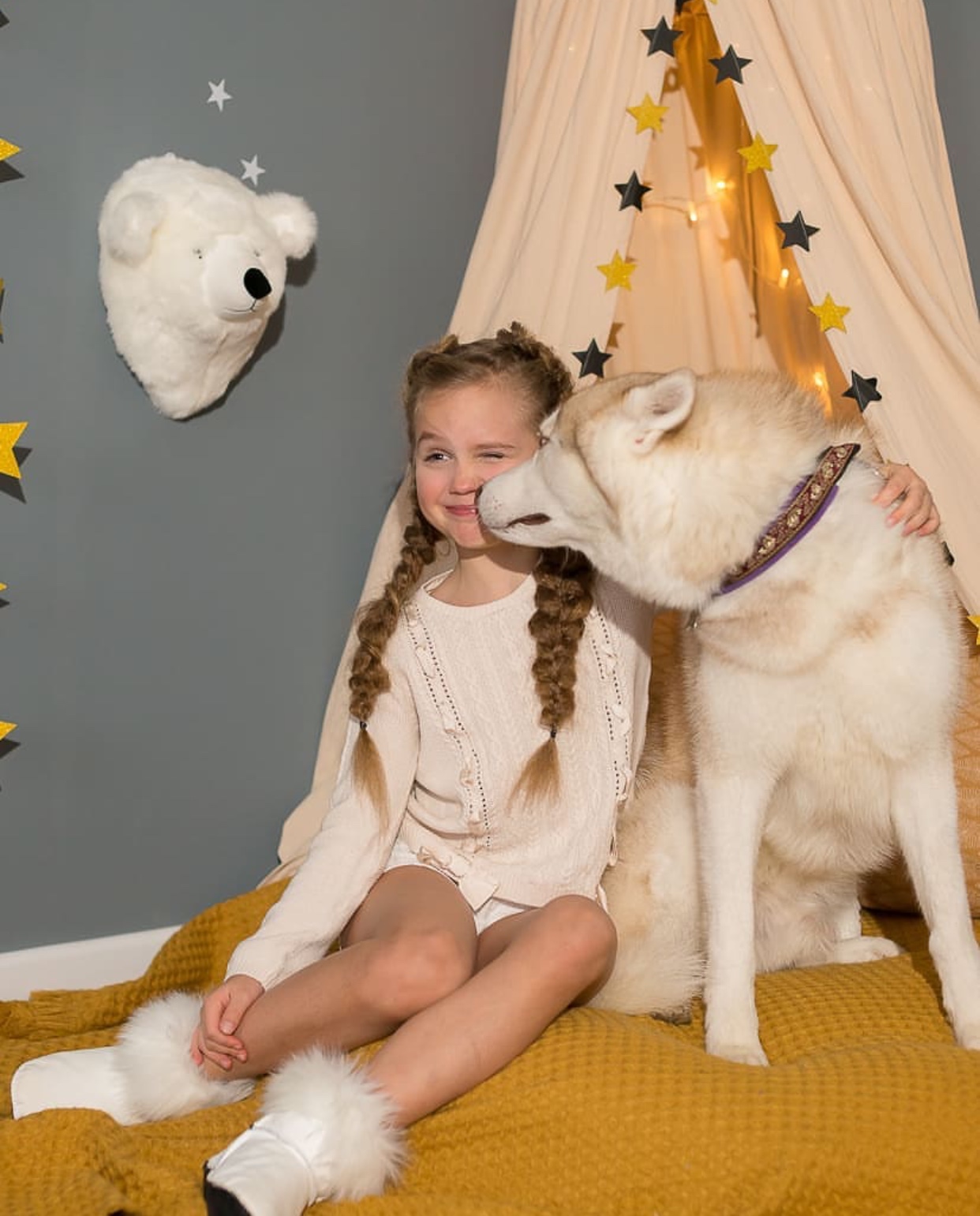 a girl sitting on the bed while a Husky kissing her cheeks