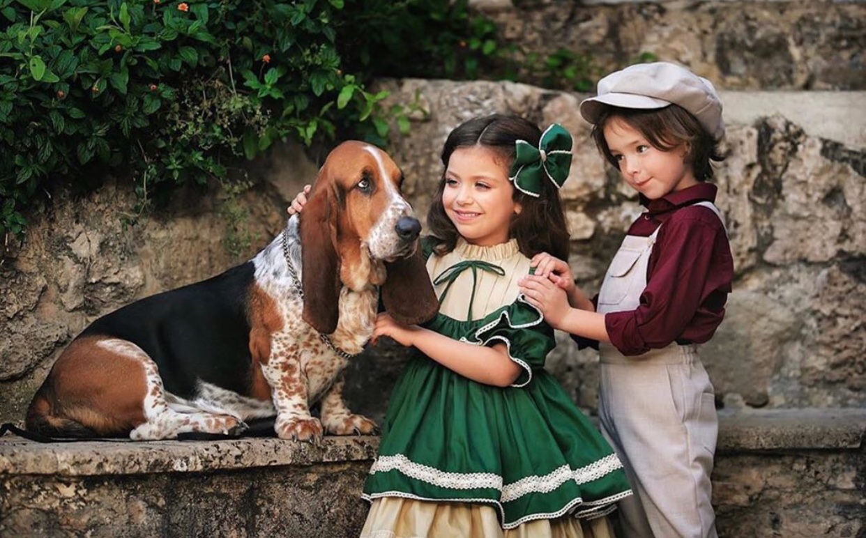 two kids looking at the Basset Hound sitting on top of the bench beside them