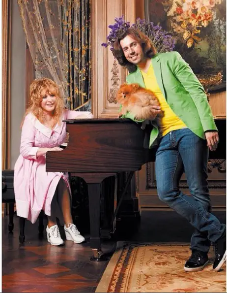Alla Pugachova on a piano while a man with a Pomeranian is leaning towards the piano