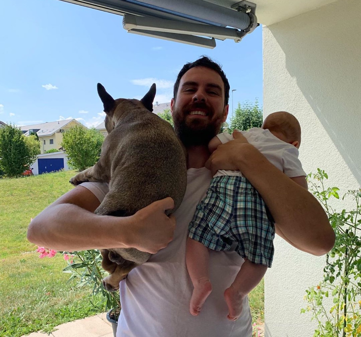 A man holding a French Bulldog and a baby on each of his arms