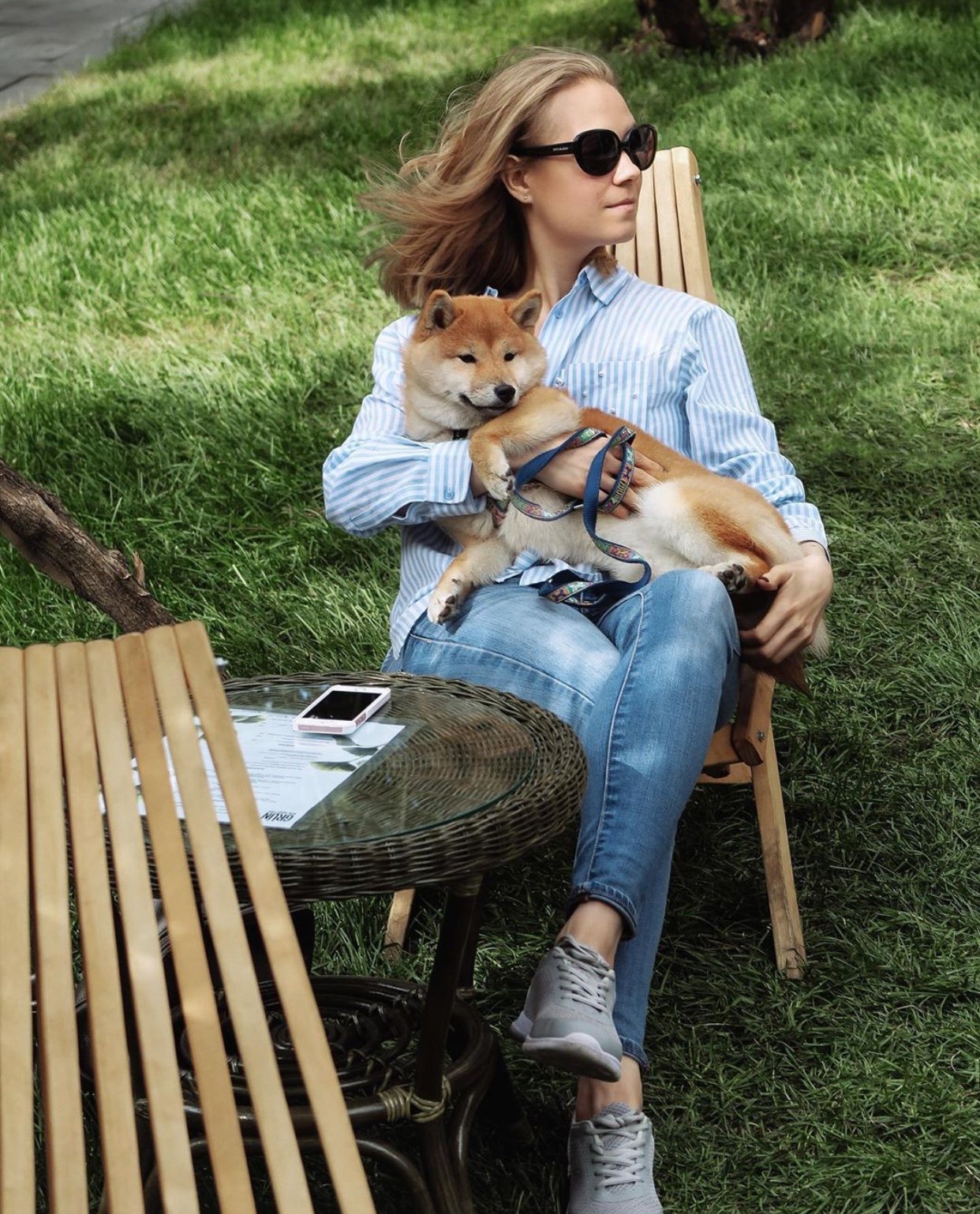 a woman sitting on the chair in the yard with her Shiba Inu pupy in her lap