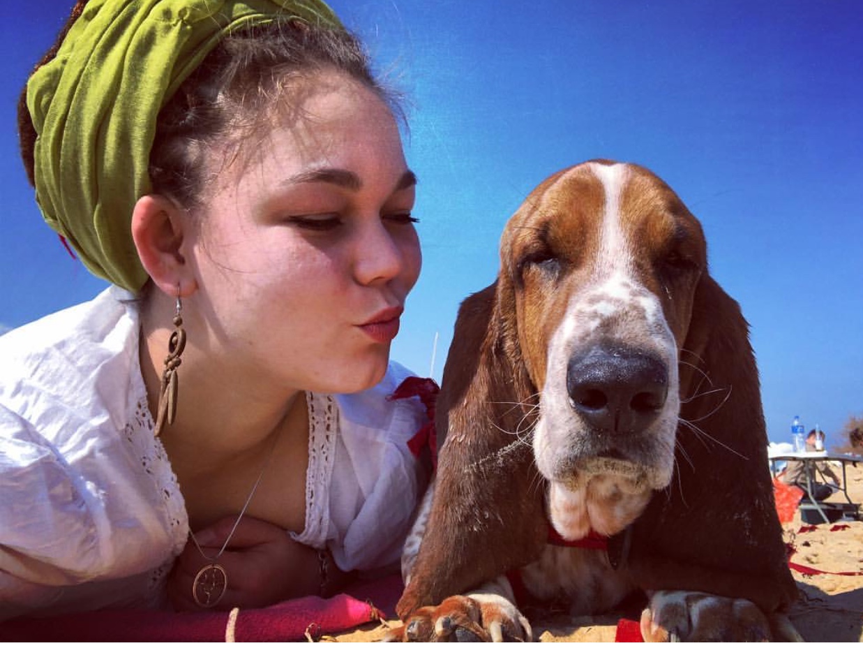 Basset Hound lying in the sand next to a woman