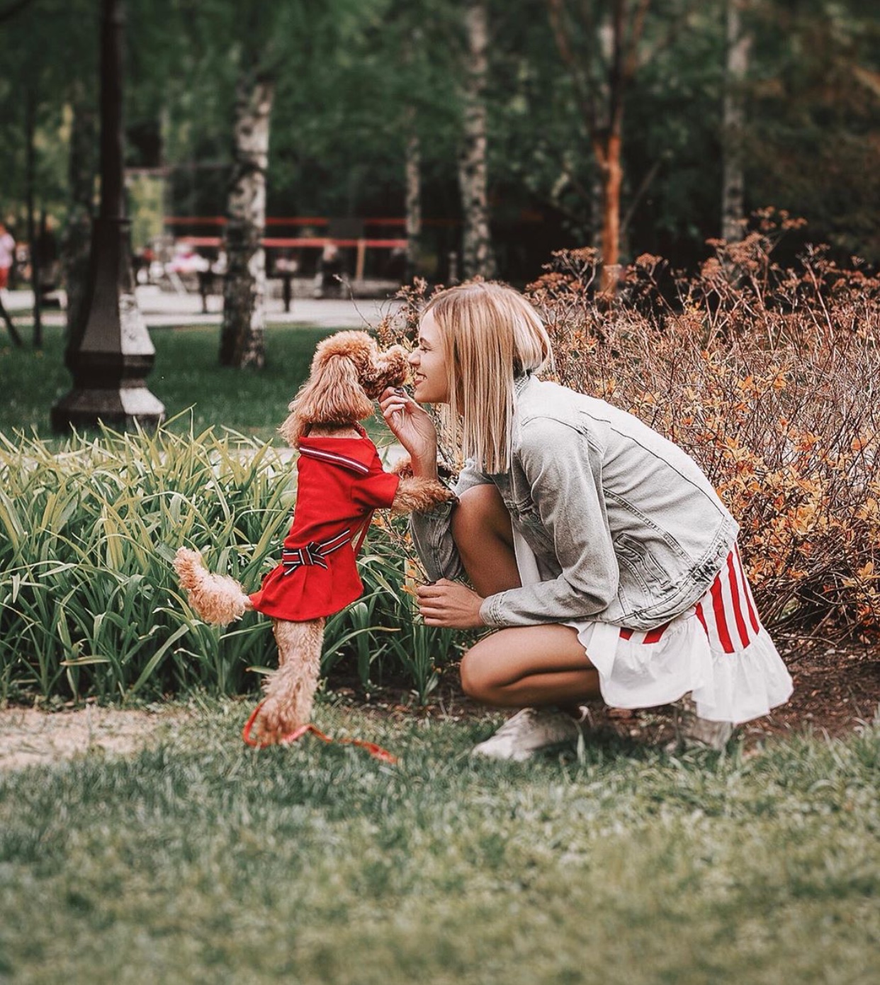 A woman at the park with her Poodle puppy wearing a red dress while standing in front of her