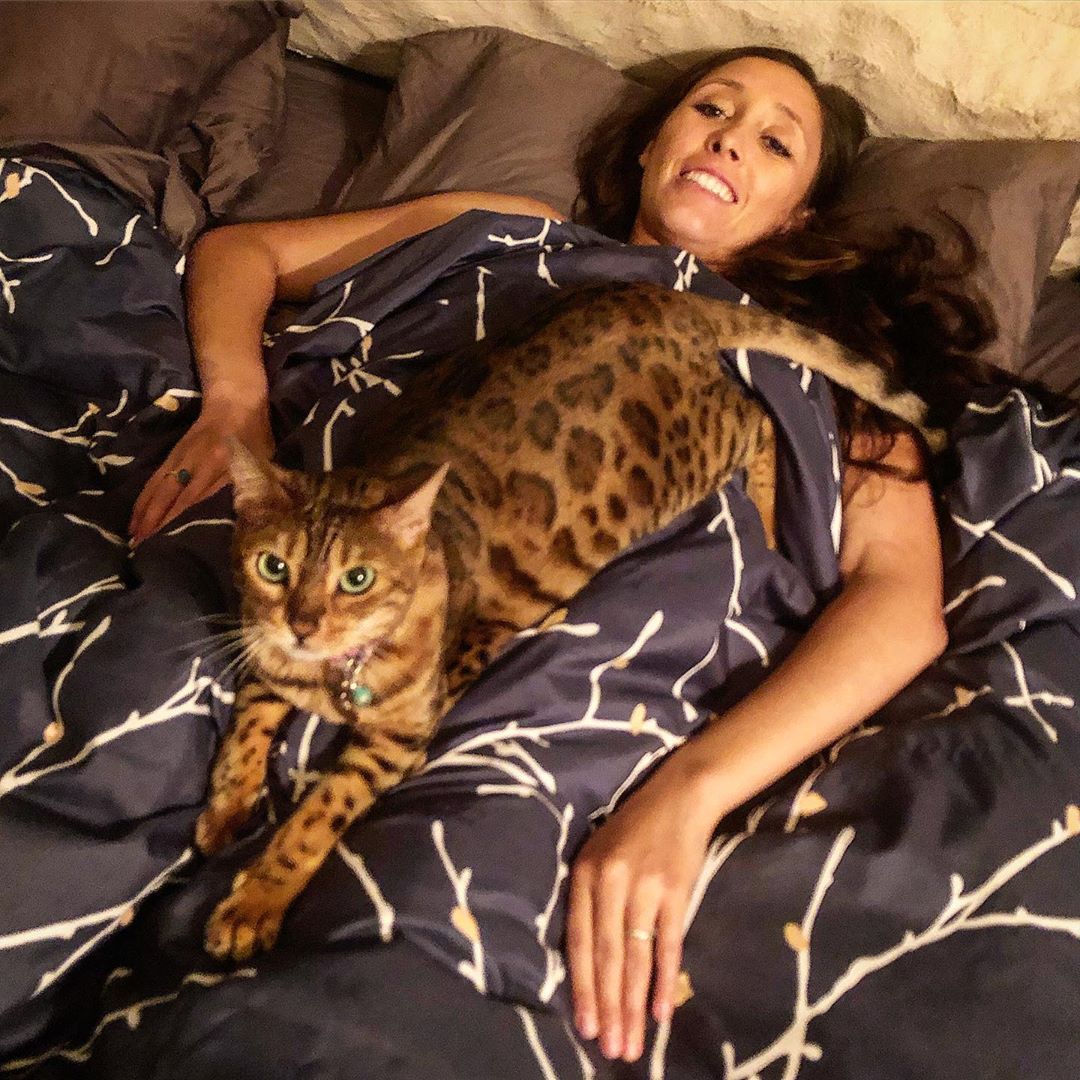 woman lying on the bed with a Bengal Cat on top of her