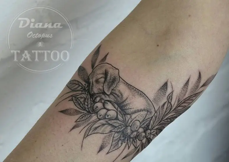 a black and gray sleeping Dachshund puppy on the bed of flowers and leaves tattoo on the forearm