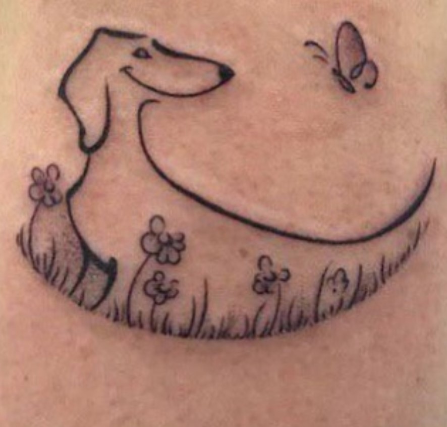 an outline of a Dachshund in the grass with flowers and a butterfly on top of it tattoo