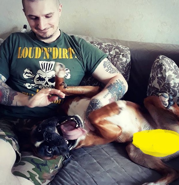 a man sitting on the couch while petting his Boxer lying next to him