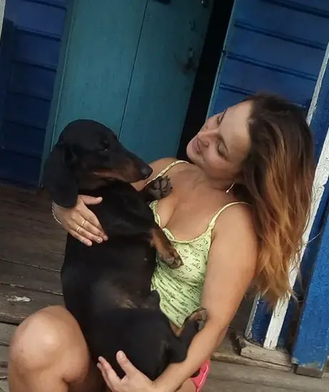 a woman sitting in the front porch while carrying her Dachshund