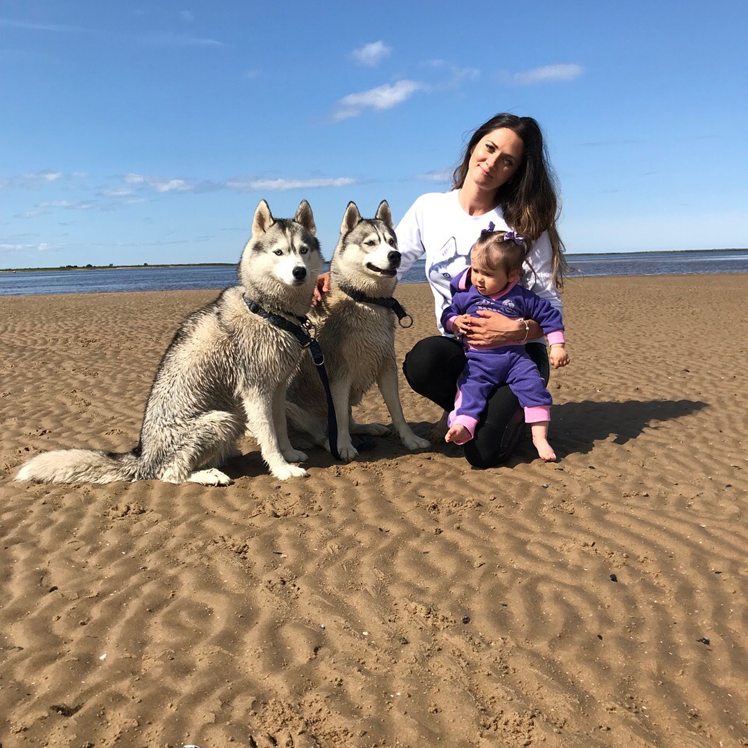 A woman with a baby at the beach with their two Huskies