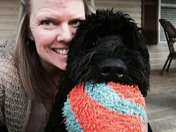 a woman taking a selfie with a Schnoodle holding a chew toy in its mouth