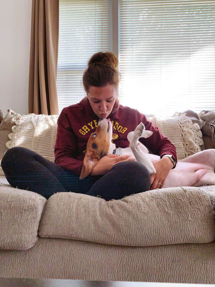 a woman sitting on couch while kissing the beagle that is lying on her lap