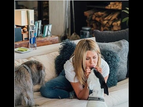Jennifer Annisto siting on the couch while kissing her pitbull sitting on the floor in front of her