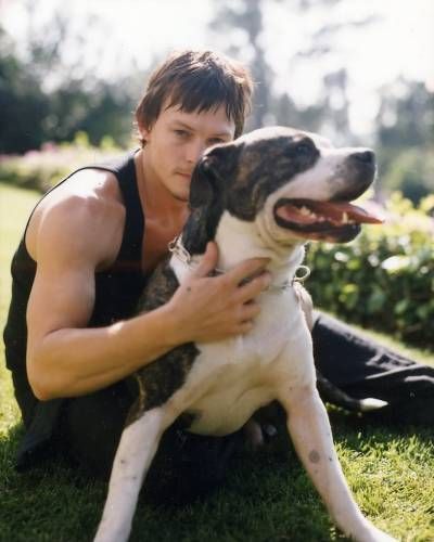 Norman Reedus sitting in the yard behind his pitbull
