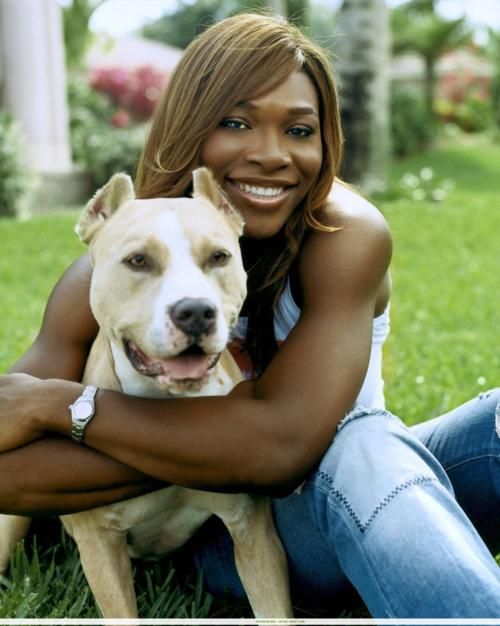 Serena Williams sitting on the grass while hugging her pitbull