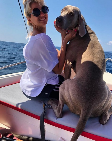 A Weimaraner sitting on the boat next to a woman