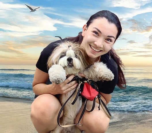 A woman sitting by the beach while holding a Shih Tzu