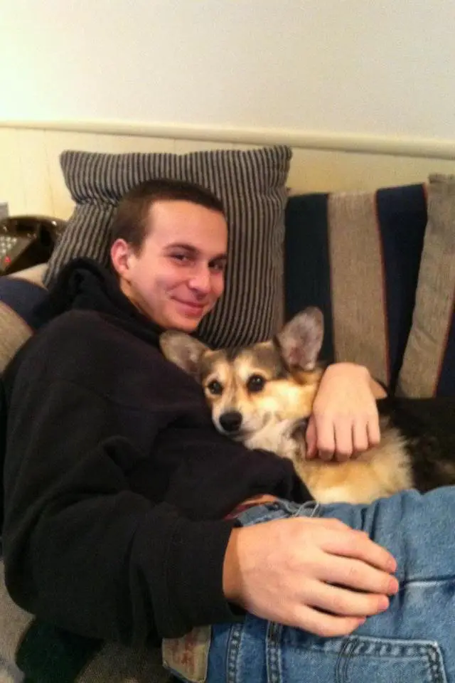 A man sitting on the couch with his corgi