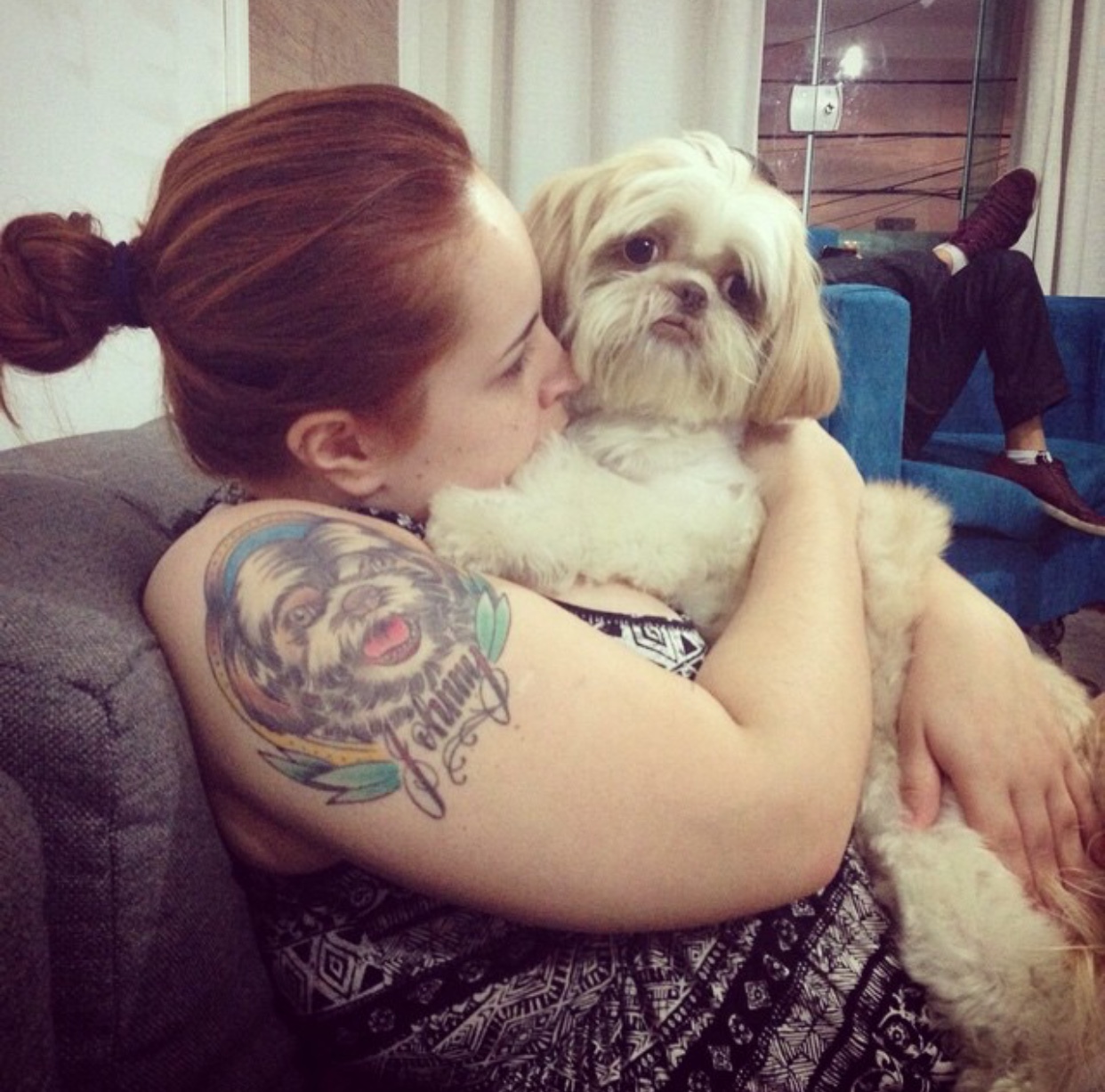 girl kissing its Shih Tzu with its face tattoo on her shoulder