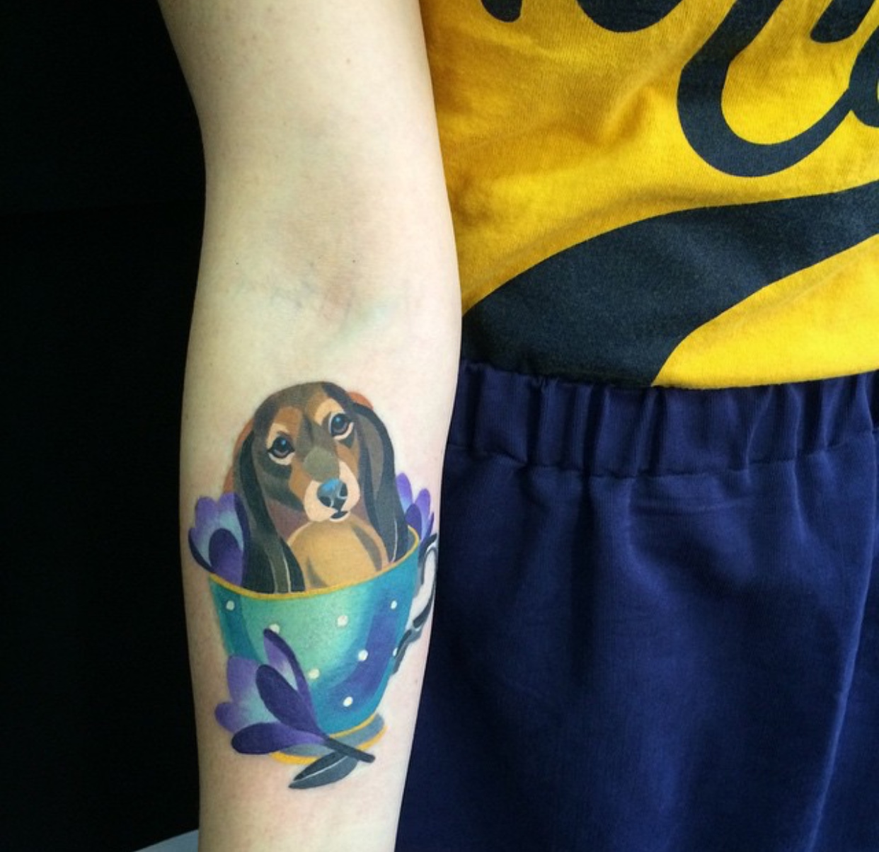 Dachshund in cup tattoo on arm