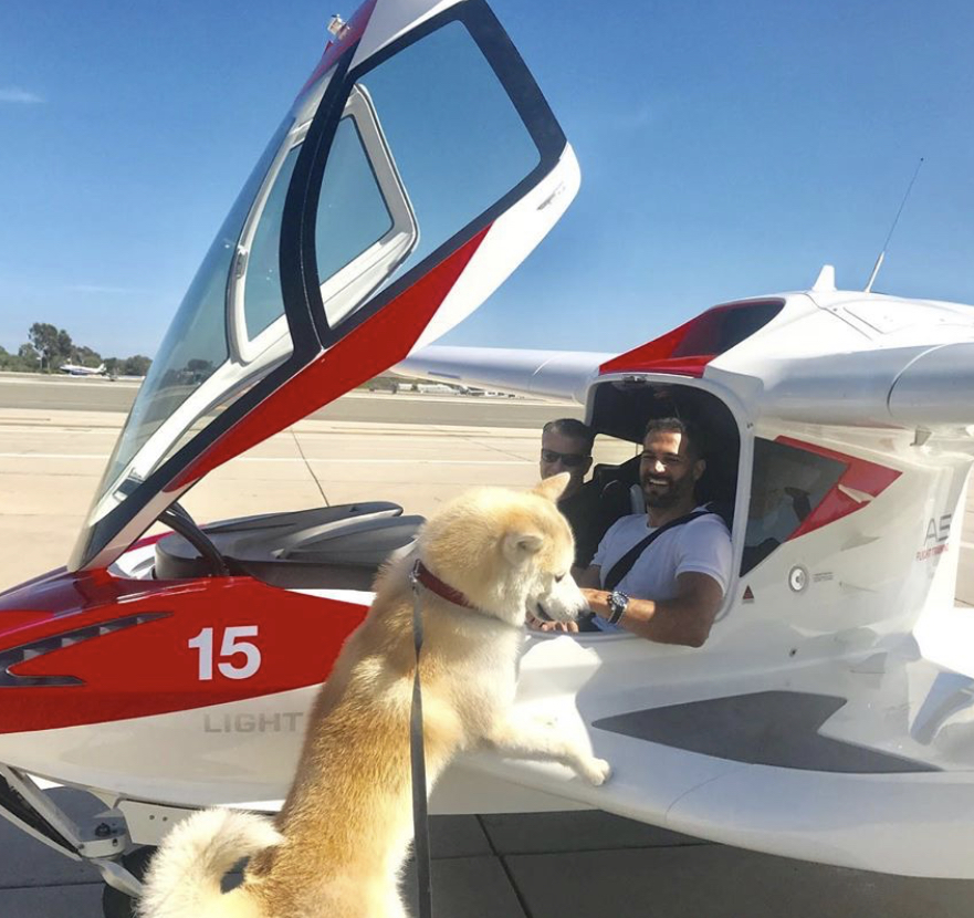 Akita Inu standing up leaning against the small plane with two people