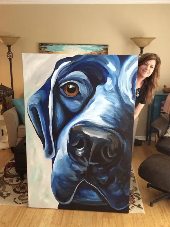 a painter standing behind her large painting of the face of a black Labrador Retriever