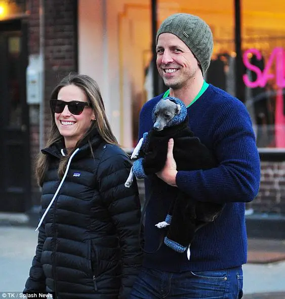 Seth Meyers holding his Greyhound dog while walking in the street with a woman