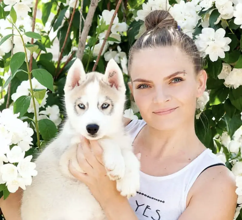 a woman with her Husky Puppy puppy standing in front of the tree with white flowers