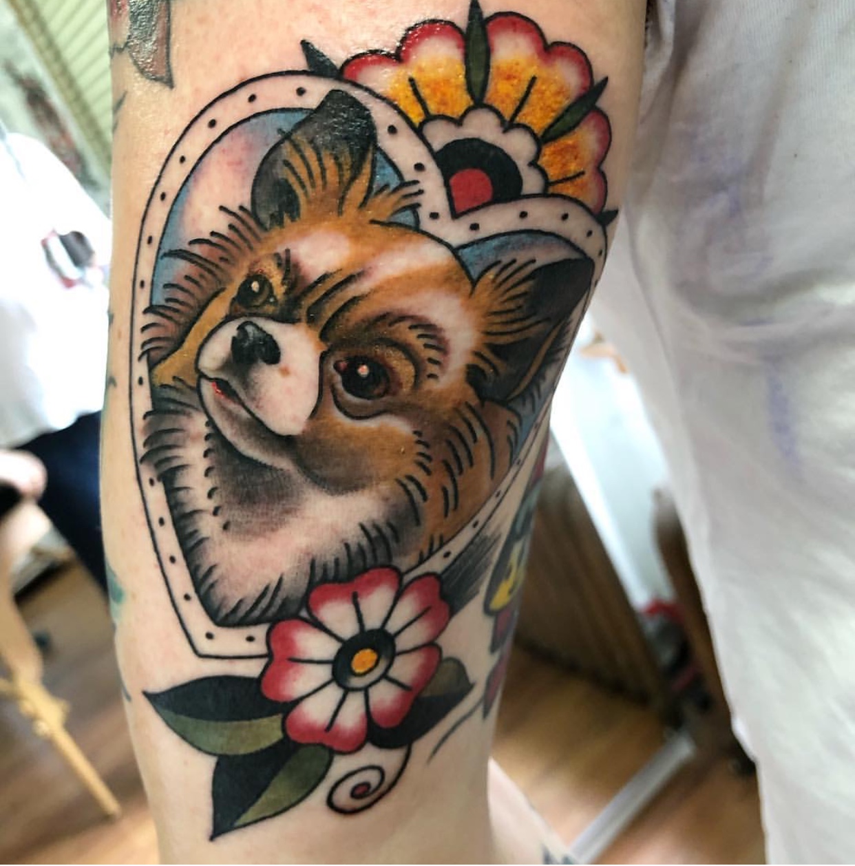 face of Pomeranian in heart shaped frame with flowers tattoo on the shoulder