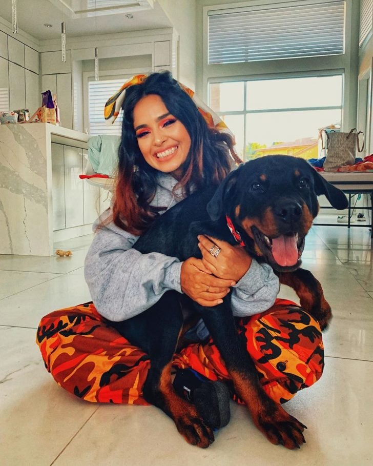 Rottweiler puppy sitting in between the legs of her owner on the floor