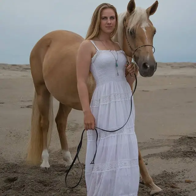 a girl in white dress with a horse behind her