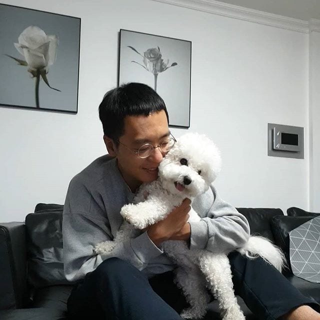 A man sitting on the couch while hugging his Bichon Frise